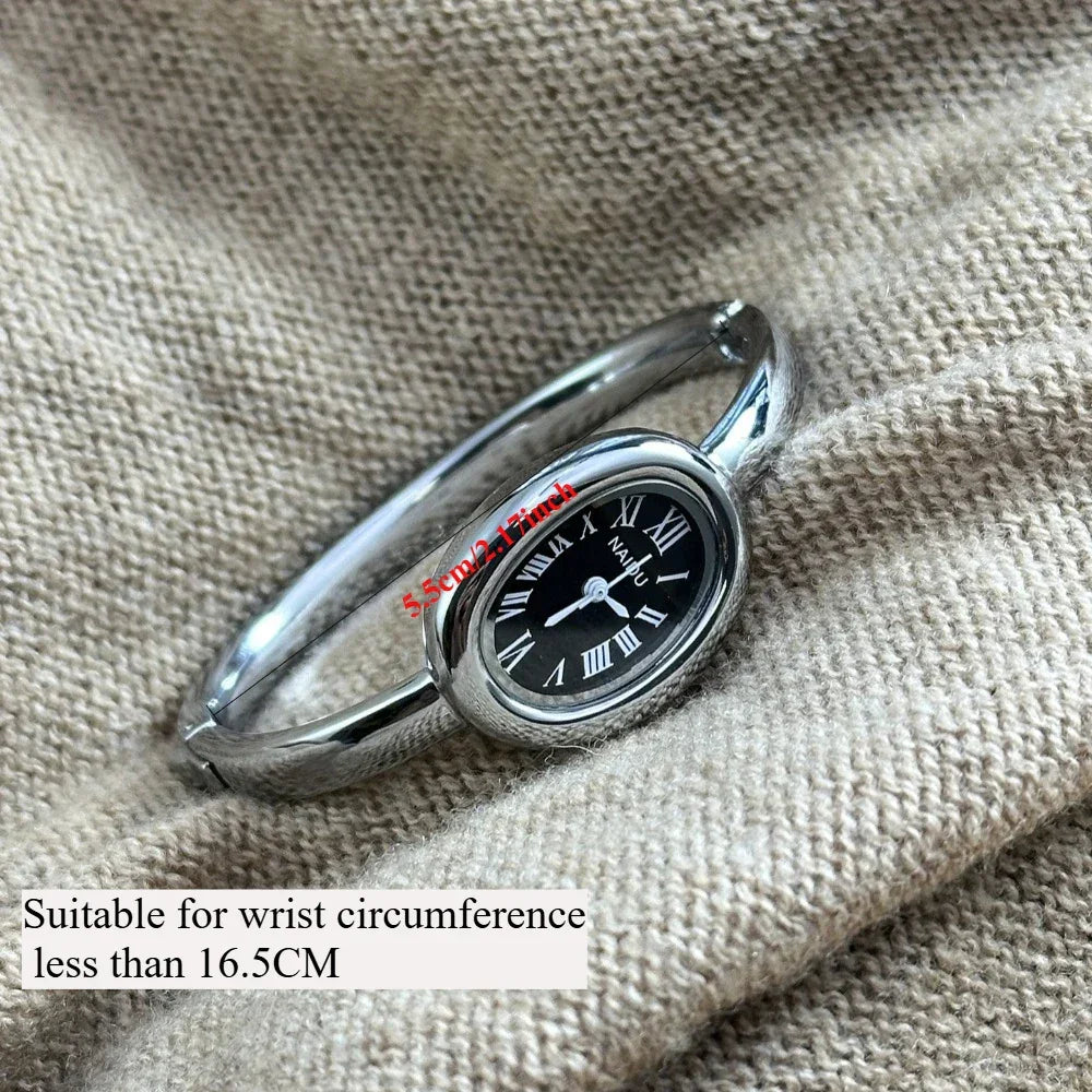 Silver bangle watch with black oval face and Roman numerals on textured beige fabric