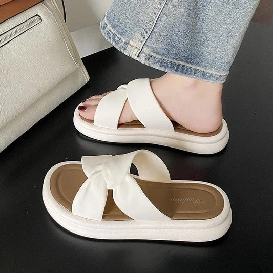 White slip-on sandals with criss-cross straps and a bow, styled with denim jeans, danastors fashion