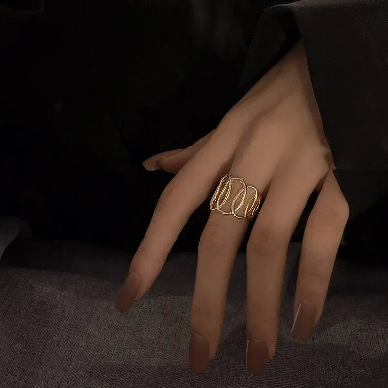 Elegant gold statement ring on woman's hand with long nude nails, modern jewelry fashion