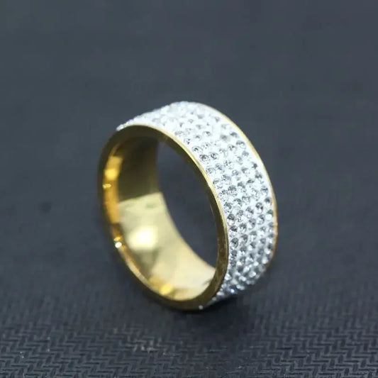 Gold wide band ring with rows of sparkling clear crystals on black textured background