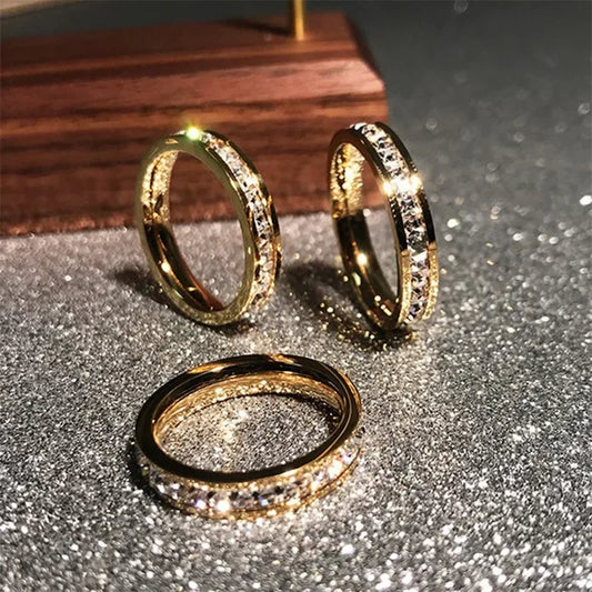 Gold rings with sparkling clear stones displayed on a glittery silver surface