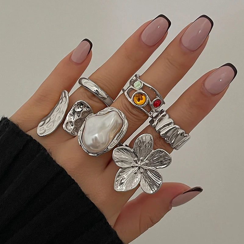 Woman's hand with French tip nails wearing silver statement rings, pearl and floral designs