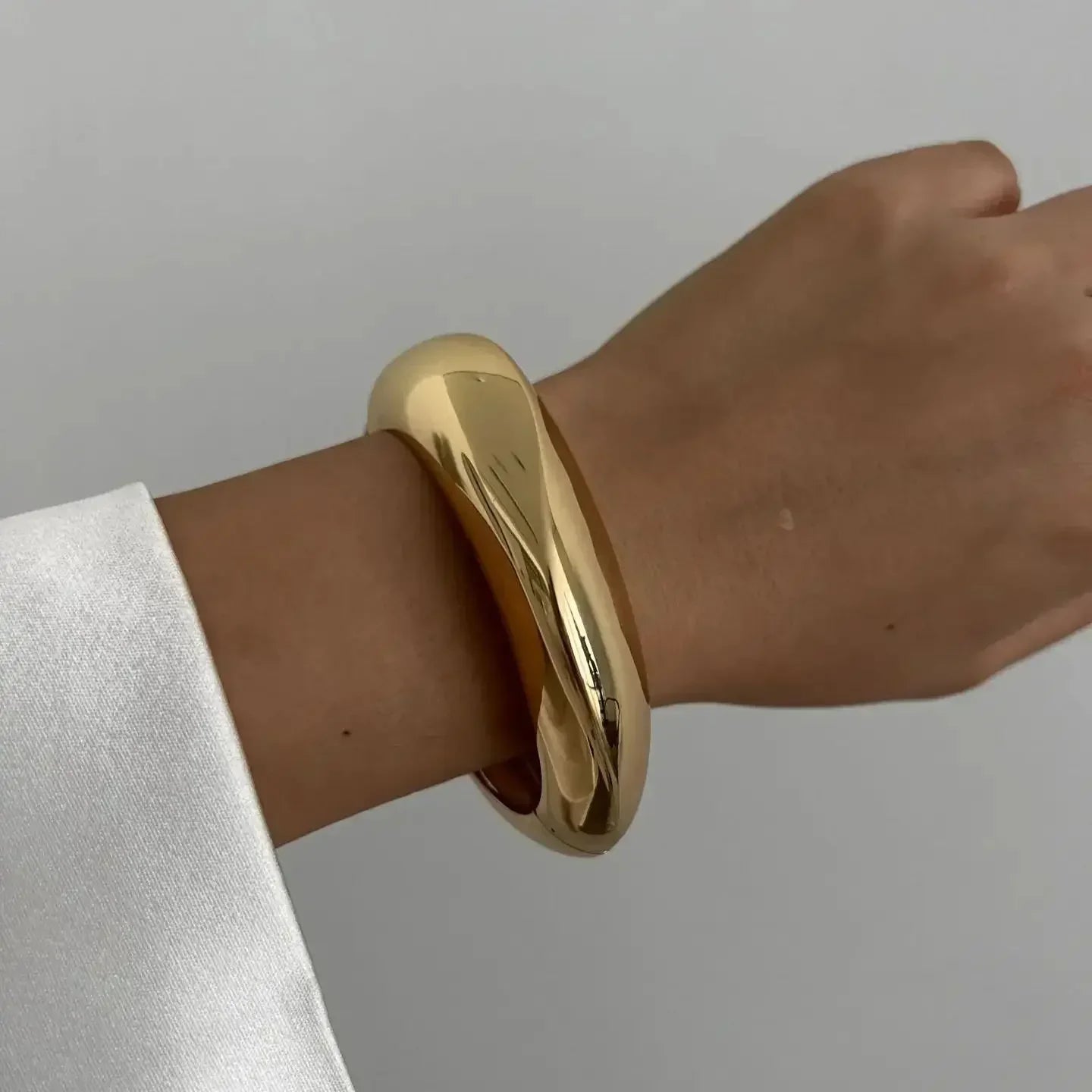 Bold gold chunky bangle bracelet on wrist, modern fashion jewelry against white background