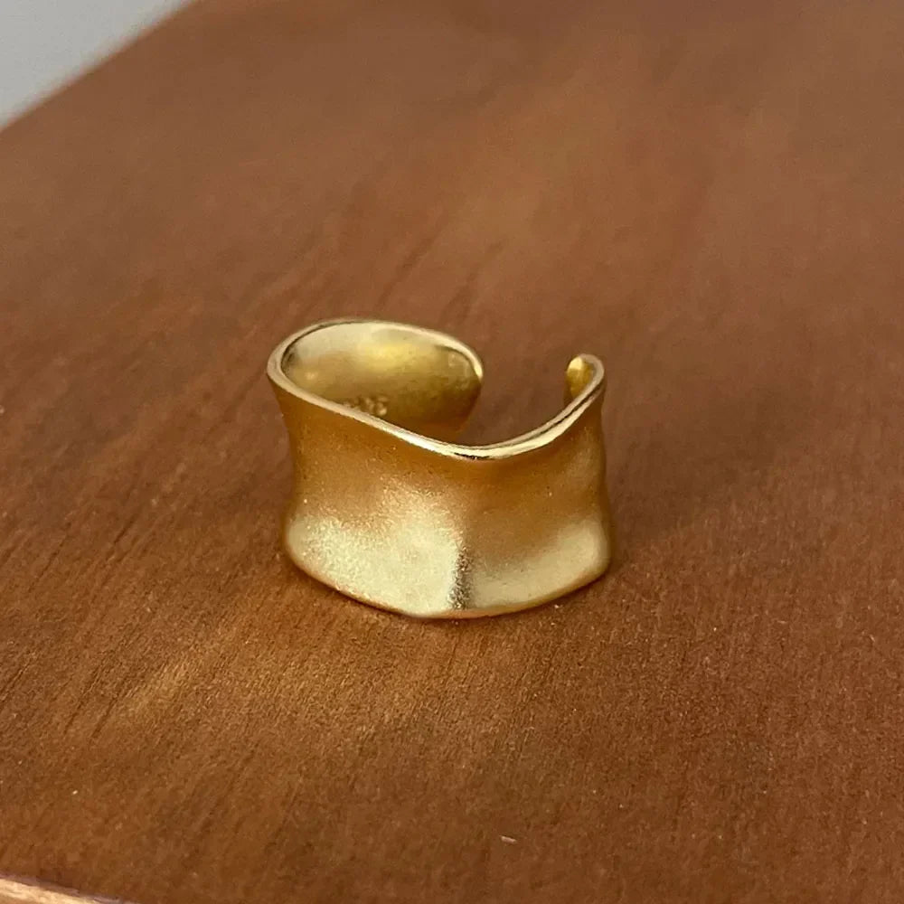 Wide gold adjustable ring with a hammered texture on a wooden surface