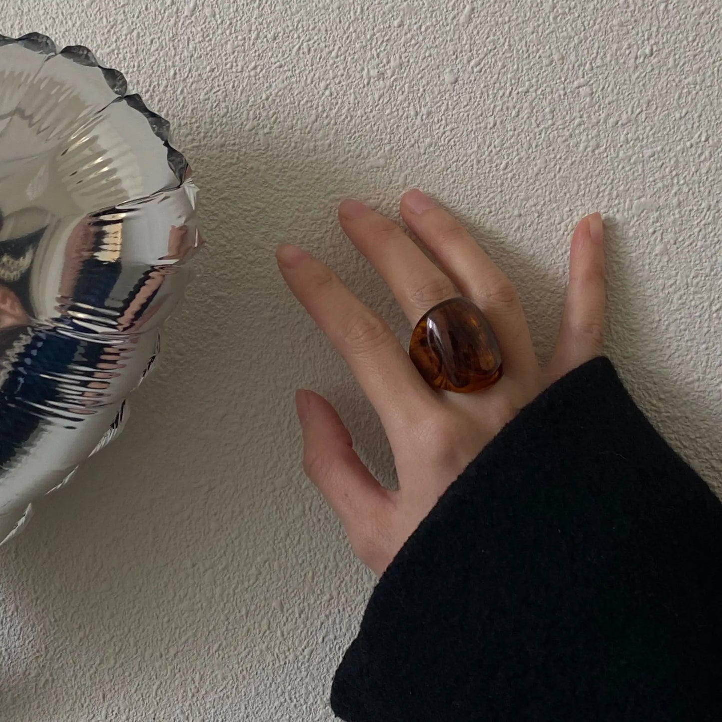 Hand wearing chunky brown resin ring and black sleeve, holding a silver balloon