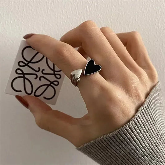 Hand wearing adjustable silver ring with black and white heart, holding card, fashion jewelry