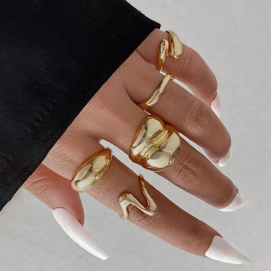 Hand wearing chunky gold statement rings with white almond-shaped nails