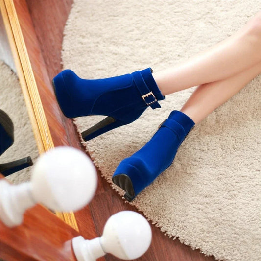 Woman wearing blue high heel ankle boots with buckle detail on cream rug, fashion footwear