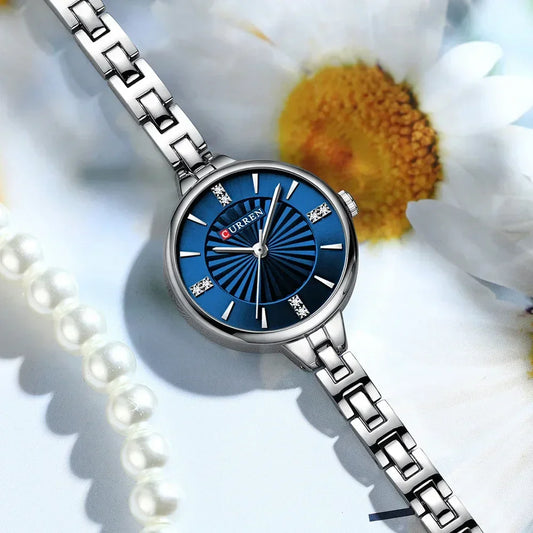 Elegant silver women’s wristwatch with blue dial, diamond accents, floral and pearl background