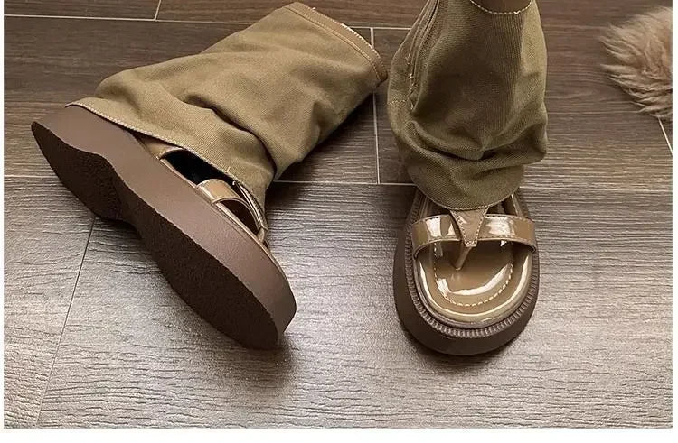 Beige platform sandals with glossy straps and khaki fabric pants on wooden floor