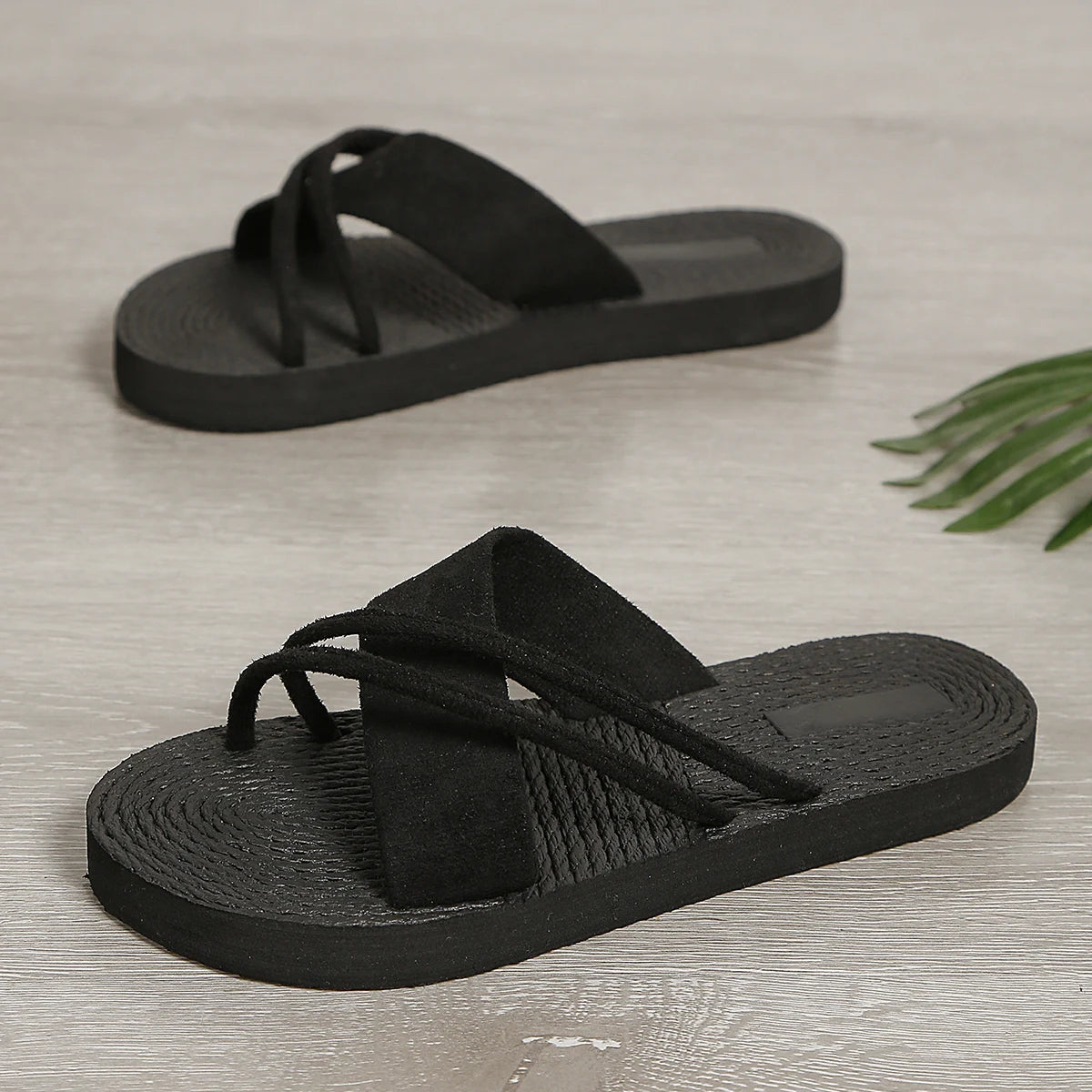 Black slip-on sandals with suede crisscross straps on a textured sole, displayed on wood floor