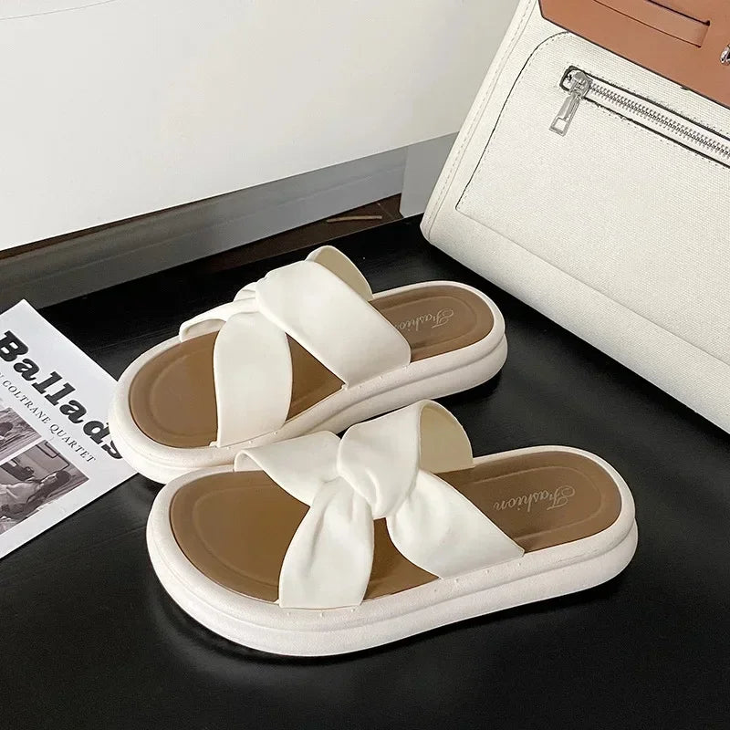White bow knot slide sandals with thick soles on a black surface beside a beige bag
