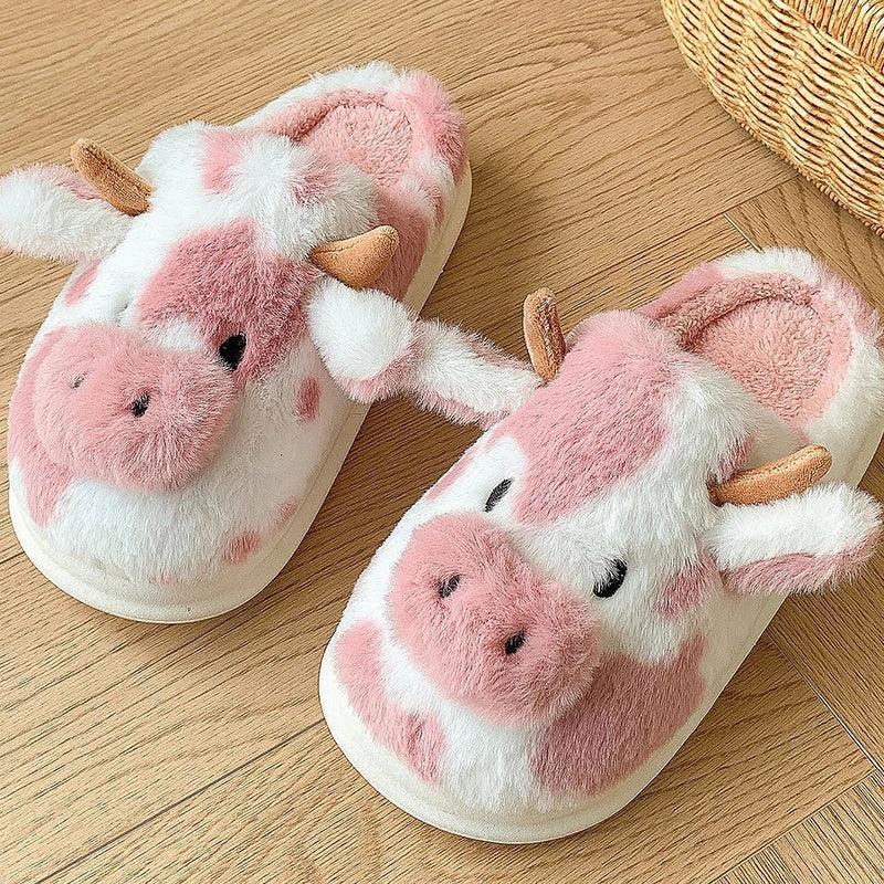 Cute pink and white cow plush slippers with horns on wooden floor, cozy home footwear