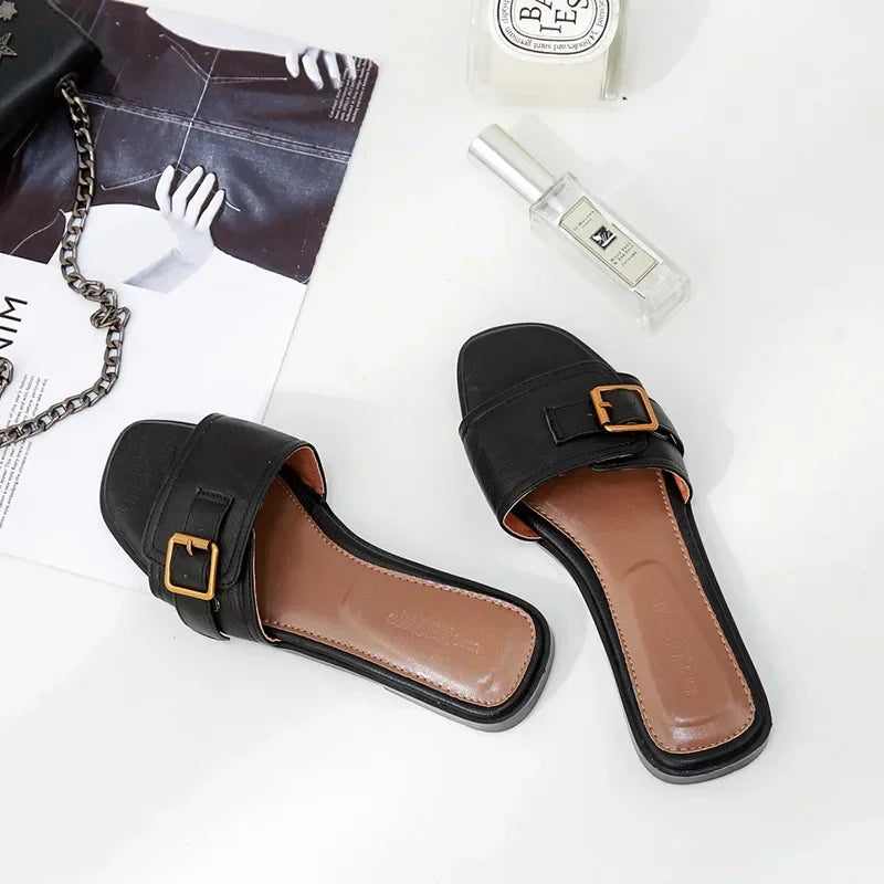 Black flat slide sandals with gold buckle and square toe on white background