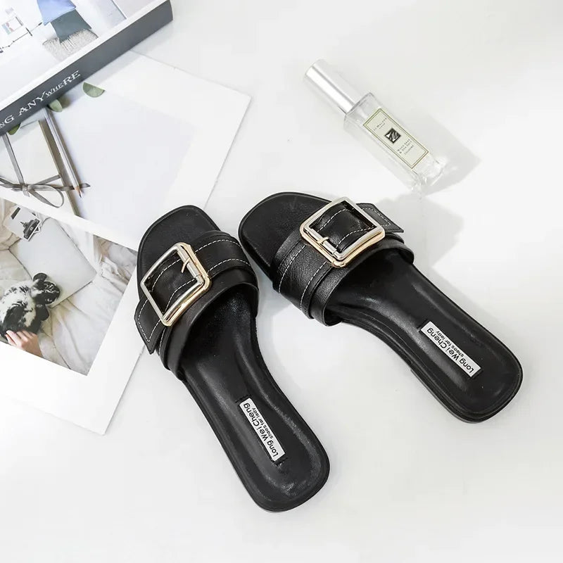 Black fashion slide sandals with gold buckles on white background, flat lay style