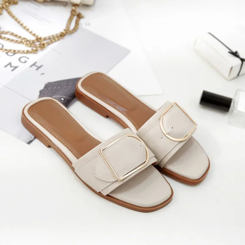 Beige flat sandals with square toes and gold buckle detail on white background