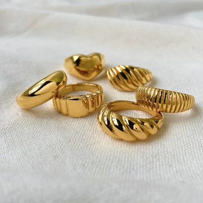 Set of chunky gold rings with smooth, textured, and heart-shaped designs on white fabric
