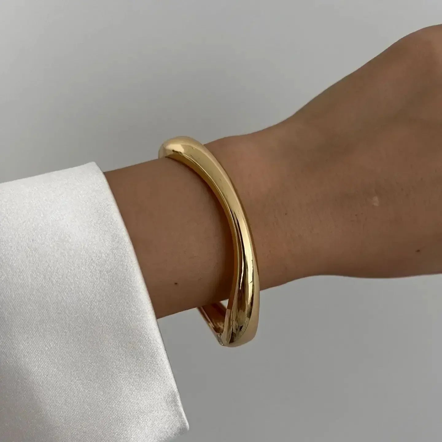 Minimalist gold bangle bracelet on wrist with white sleeve, modern jewelry