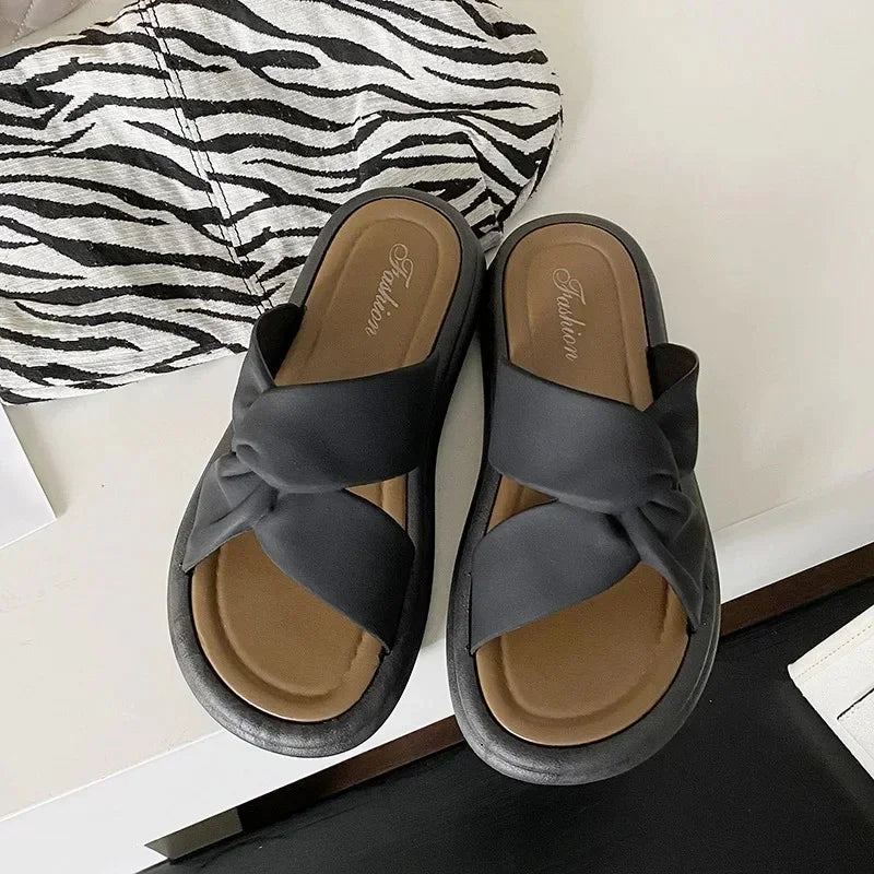 Black knot slip-on sandals with cushioned sole, next to zebra print fabric, on a table