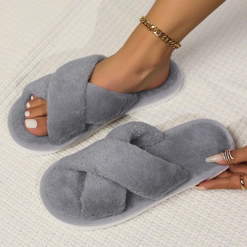 Woman wearing cozy grey faux fur cross band slippers on a textured light surface