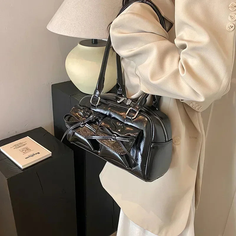 Woman in beige blazer carrying a glossy black handbag with bow detail, modern fashion accessory