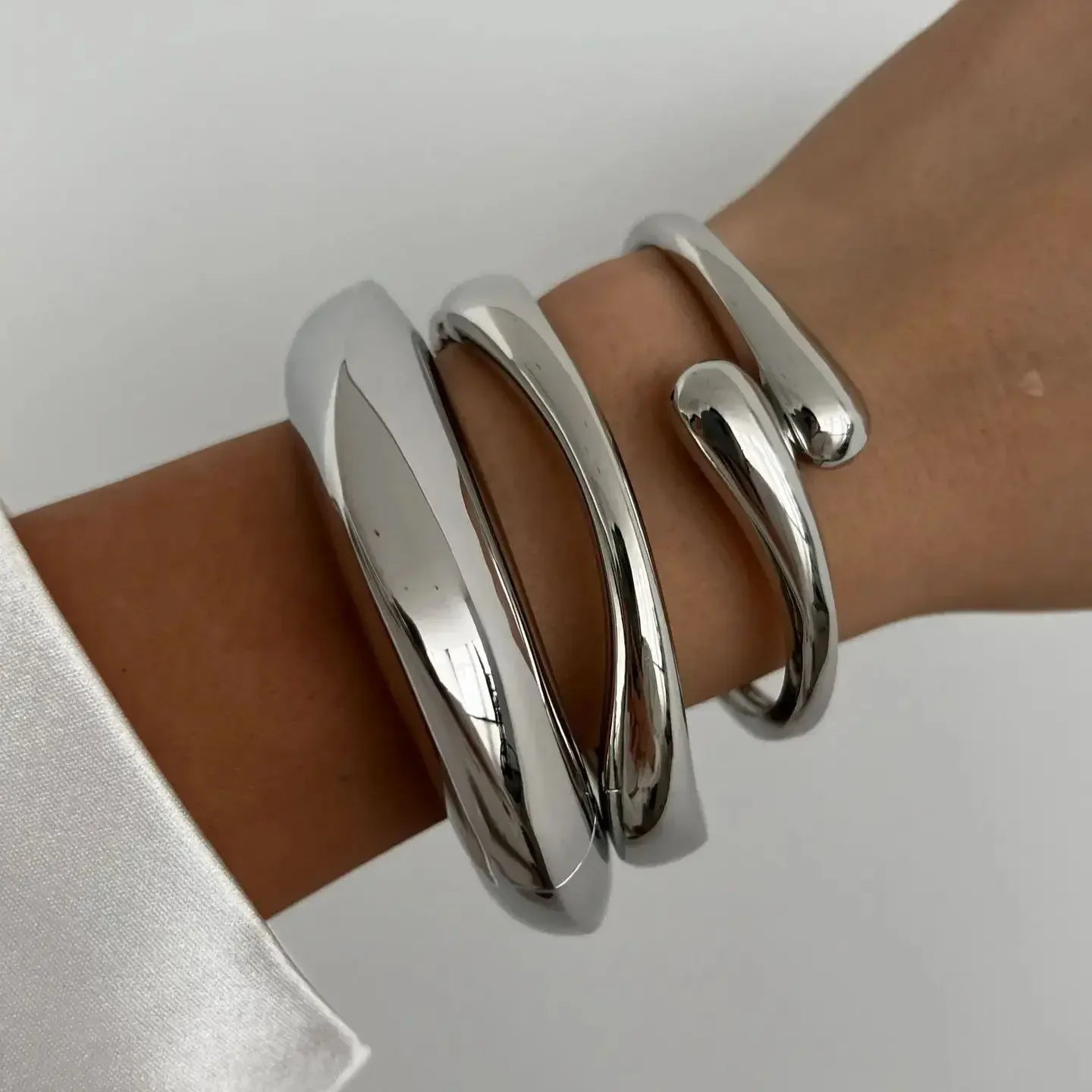 Modern chunky silver bracelets on wrist, minimalist jewelry fashion, white sleeve
