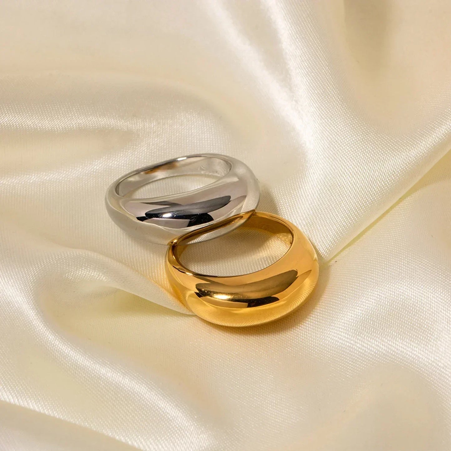 Gold and silver dome rings on smooth ivory satin fabric, modern jewelry closeup
