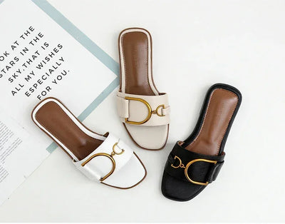 Three pairs of flat slip-on sandals in white, beige, and black with gold buckle detail, displayed on a white background.